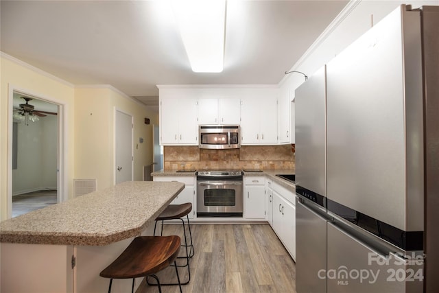 kitchen featuring light wood-type flooring, tasteful backsplash, a kitchen bar, stainless steel appliances, and crown molding