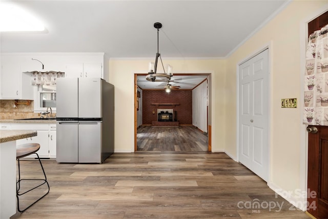 interior space with white cabinets, a fireplace, fridge, light wood-type flooring, and decorative light fixtures