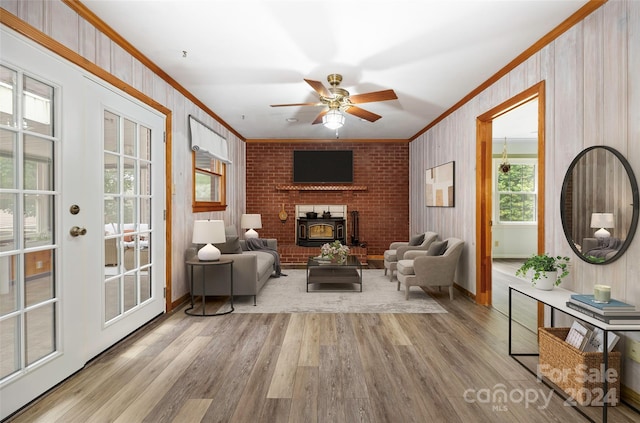 living room featuring a brick fireplace, a wood stove, light wood-type flooring, crown molding, and ceiling fan