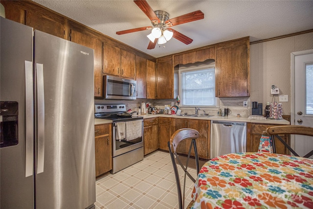 kitchen with ceiling fan, a textured ceiling, stainless steel appliances, and sink