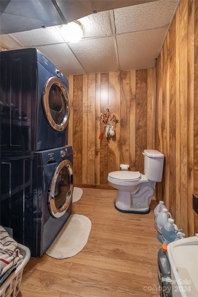 washroom with stacked washer / drying machine, wood walls, and wood-type flooring