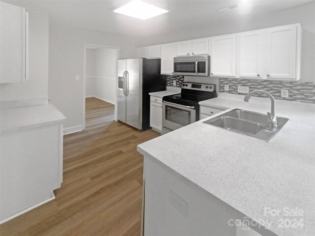 kitchen with backsplash, appliances with stainless steel finishes, sink, white cabinetry, and light wood-type flooring