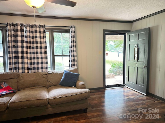 interior space featuring ceiling fan, a textured ceiling, wooden walls, dark wood-type flooring, and crown molding