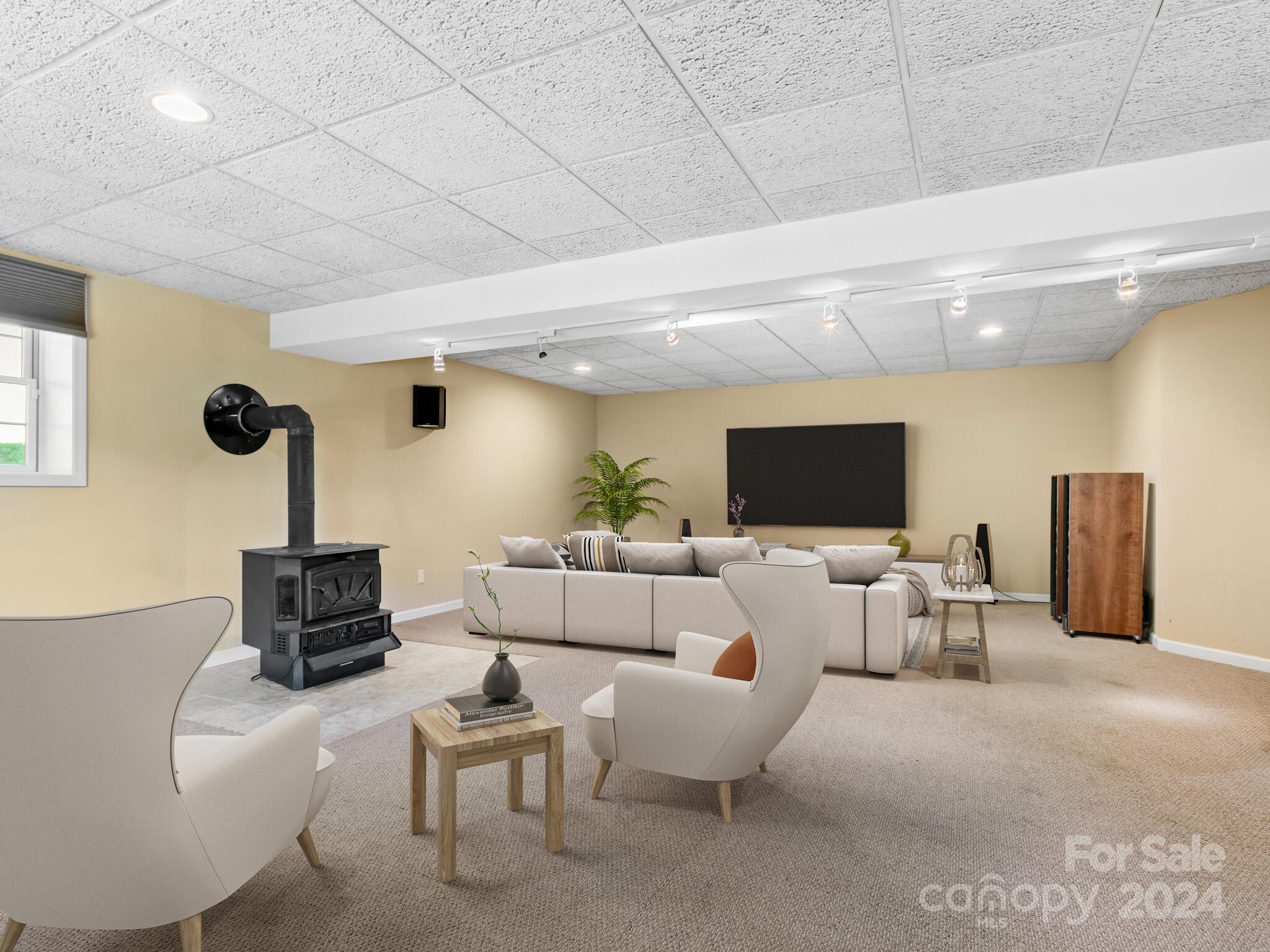 carpeted living room featuring a wood stove and a drop ceiling