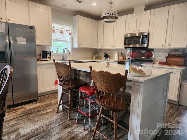 kitchen with decorative light fixtures, a kitchen island, white cabinetry, and appliances with stainless steel finishes