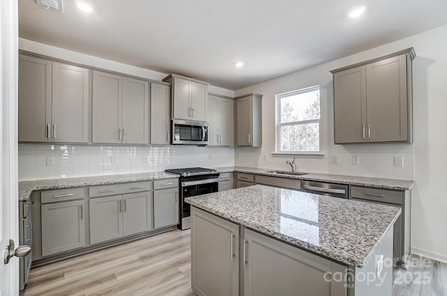 kitchen featuring sink, gray cabinetry, tasteful backsplash, light stone counters, and appliances with stainless steel finishes