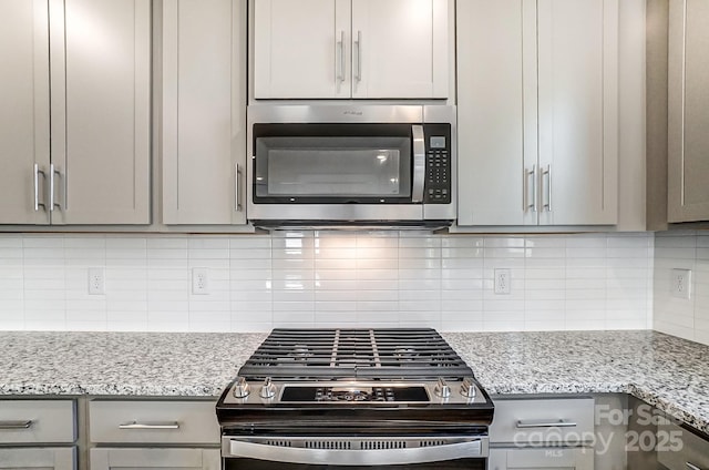 kitchen with tasteful backsplash, light stone counters, gray cabinets, and appliances with stainless steel finishes