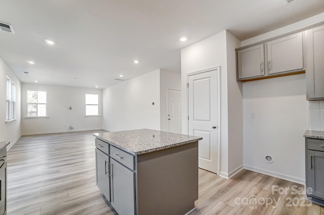 kitchen with gray cabinetry, light stone countertops, and a center island