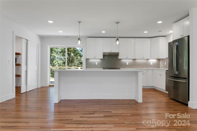 kitchen featuring light wood-type flooring, white cabinets, hanging light fixtures, and stainless steel refrigerator