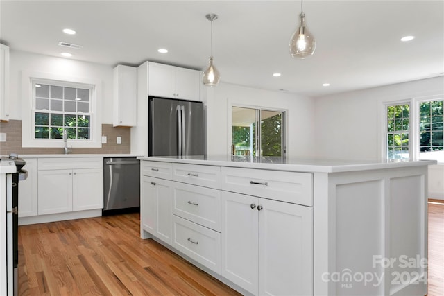 kitchen featuring light wood-type flooring, stainless steel appliances, white cabinets, and hanging light fixtures