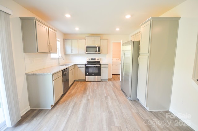 kitchen with light stone countertops, light wood finished floors, stainless steel appliances, and a sink
