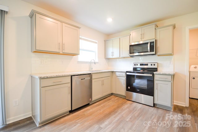 kitchen with stainless steel appliances, light wood-style flooring, a sink, tasteful backsplash, and washer / dryer