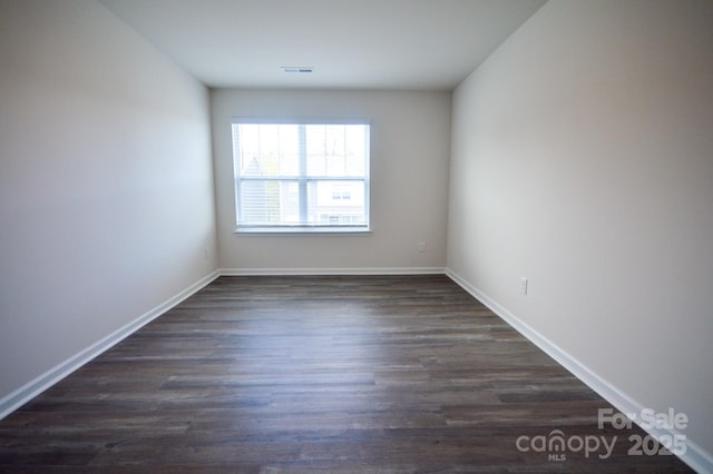 spare room with dark wood finished floors, visible vents, and baseboards