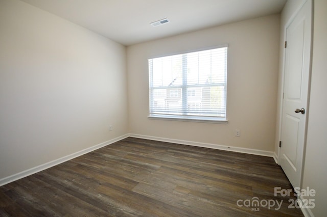 empty room featuring baseboards, dark wood-type flooring, and visible vents