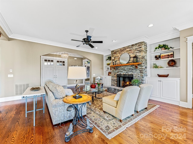 living room with ornamental molding, wood-type flooring, ceiling fan, and a stone fireplace