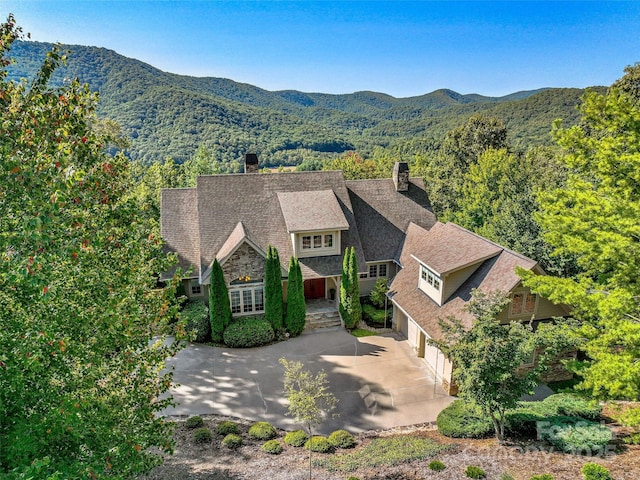 view of front of property with a garage, concrete driveway, a chimney, and a mountain view