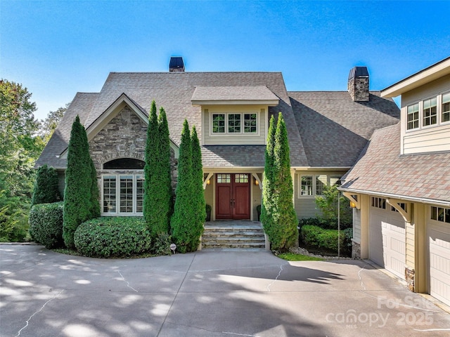 view of front of home featuring a garage, stone siding, driveway, and a chimney