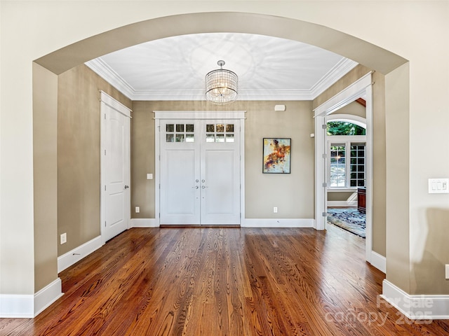 entryway with arched walkways, dark wood-style flooring, crown molding, and baseboards