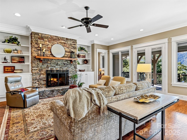 living area with built in features, ornamental molding, wood finished floors, a stone fireplace, and recessed lighting