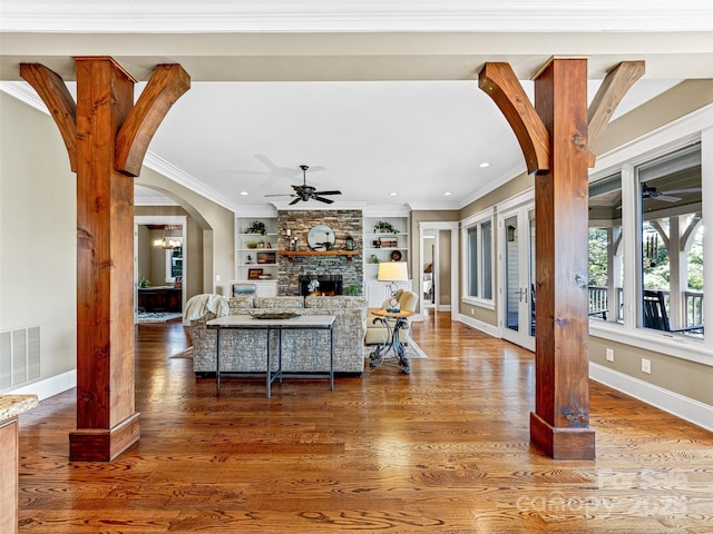 living room with arched walkways, a stone fireplace, wood finished floors, visible vents, and crown molding