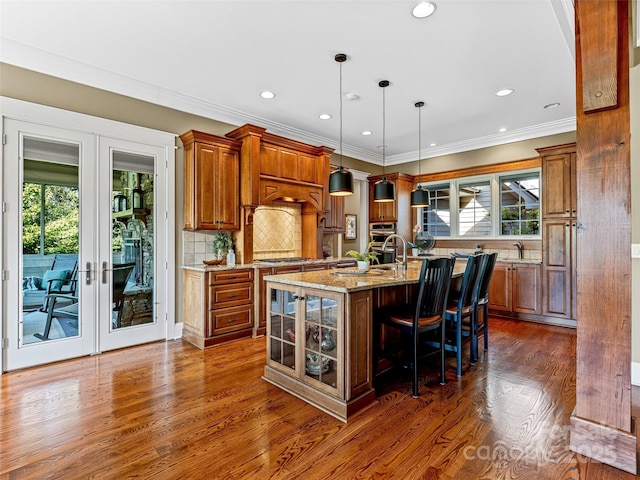 kitchen with a center island with sink, a breakfast bar, hanging light fixtures, light stone countertops, and french doors