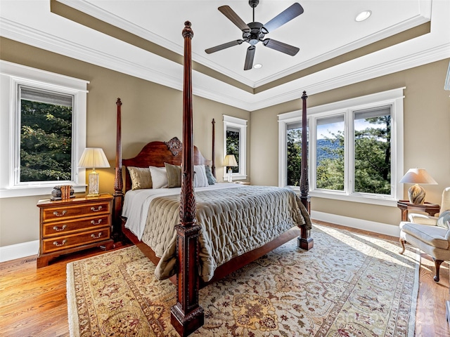 bedroom with light wood finished floors, ornamental molding, and a raised ceiling