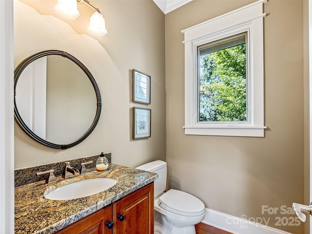 half bathroom with vanity, toilet, and baseboards