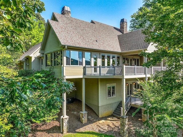 rear view of property with a shingled roof, a chimney, and a deck