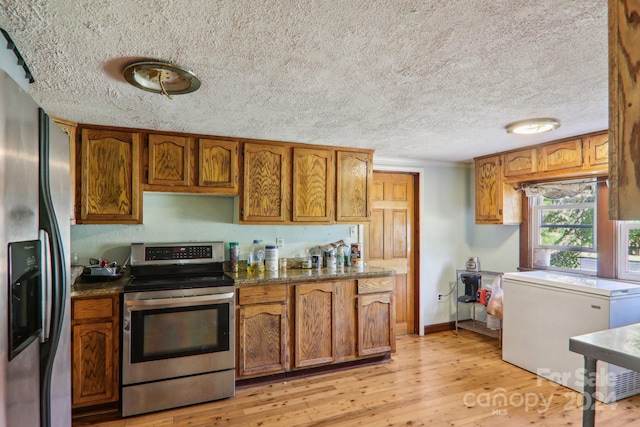 kitchen with a textured ceiling, light hardwood / wood-style flooring, appliances with stainless steel finishes, and dark stone counters