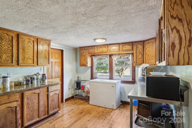 kitchen with a textured ceiling, fridge, dark stone counters, and light hardwood / wood-style floors