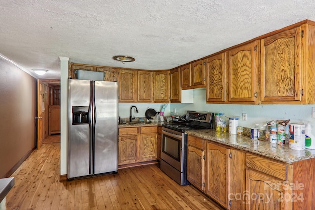 kitchen with light hardwood / wood-style flooring, stainless steel appliances, sink, dark stone counters, and a textured ceiling