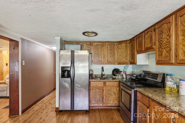 kitchen with dark stone countertops, light wood-type flooring, appliances with stainless steel finishes, sink, and a textured ceiling