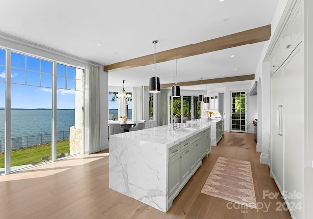 kitchen featuring a large island with sink, light hardwood / wood-style flooring, light stone counters, and decorative light fixtures