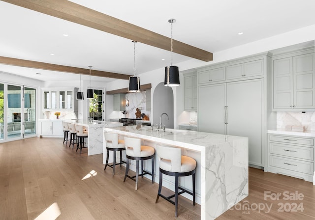 kitchen with light hardwood / wood-style flooring, beam ceiling, hanging light fixtures, decorative backsplash, and a large island