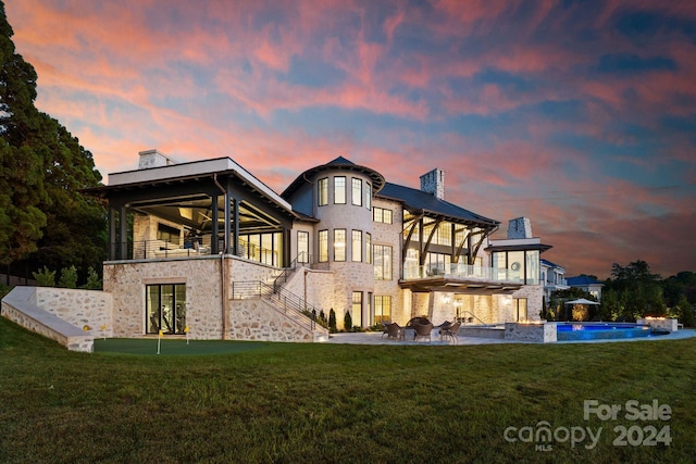 back house at dusk featuring a balcony and a lawn