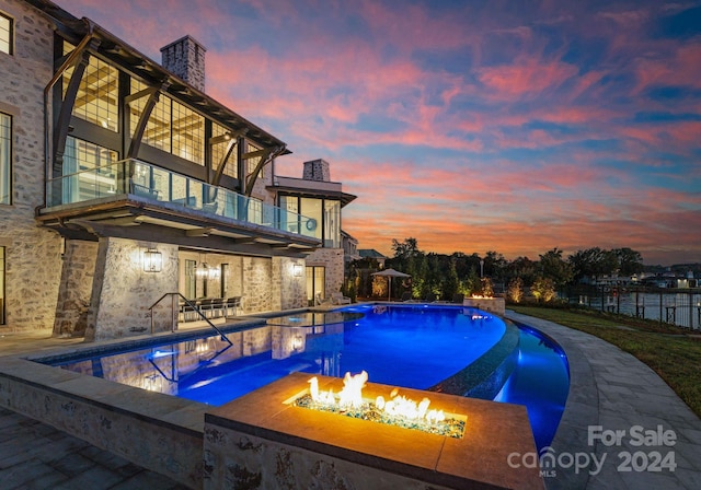 pool at dusk with a patio and a fire pit