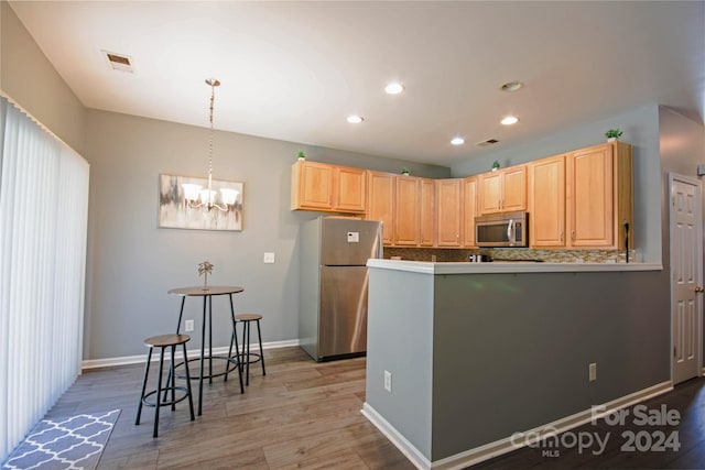 kitchen featuring light wood-type flooring, a chandelier, decorative light fixtures, stainless steel appliances, and light brown cabinets