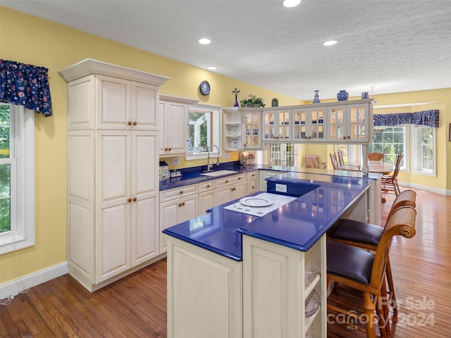 kitchen with a kitchen bar, sink, wood-type flooring, a kitchen island, and a textured ceiling