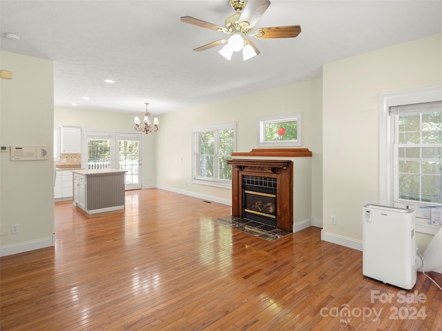 unfurnished living room with a tiled fireplace, ceiling fan with notable chandelier, and light hardwood / wood-style floors