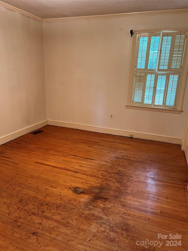 empty room with a textured ceiling, ornamental molding, and dark hardwood / wood-style floors