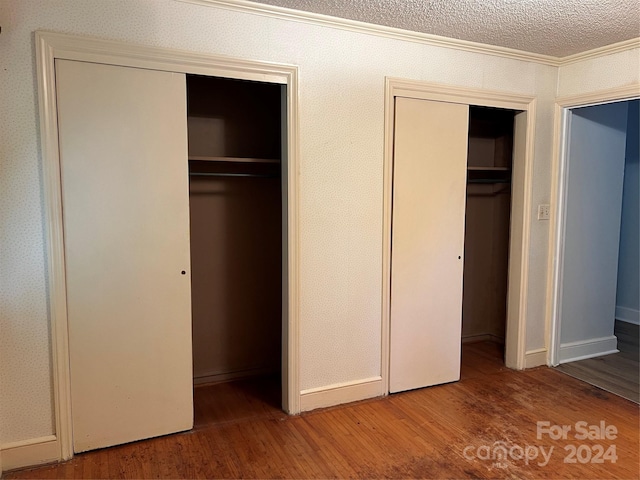 unfurnished bedroom featuring crown molding, hardwood / wood-style floors, and multiple closets