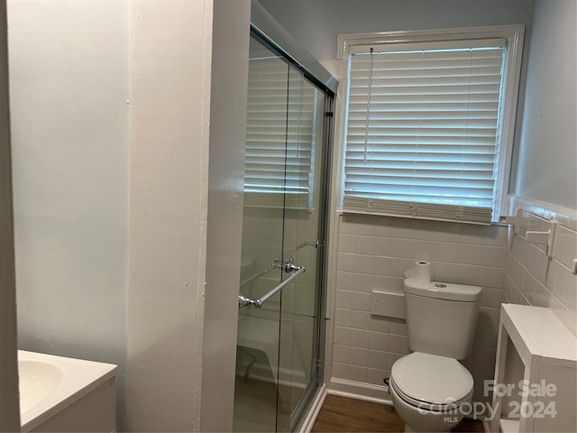 bathroom with toilet, hardwood / wood-style floors, a shower with door, vanity, and tile walls