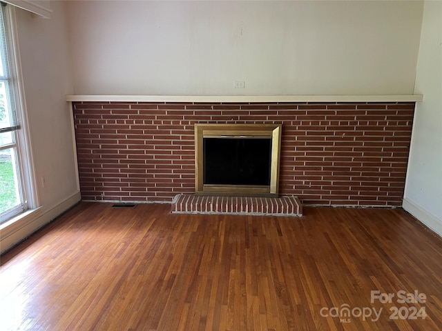 unfurnished living room featuring wood-type flooring and a brick fireplace