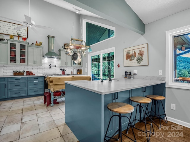 kitchen with a breakfast bar area, lofted ceiling, kitchen peninsula, wall chimney exhaust hood, and ceiling fan