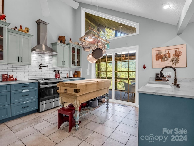 kitchen featuring backsplash, wall chimney exhaust hood, light tile patterned floors, stainless steel stove, and a textured ceiling