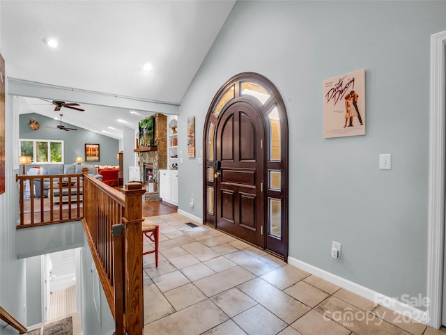 entrance foyer featuring lofted ceiling, ceiling fan, a fireplace, and light tile patterned floors