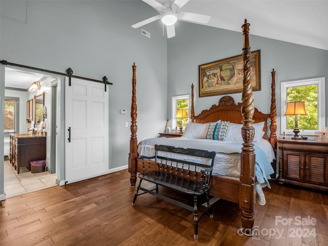 bedroom with a barn door, high vaulted ceiling, ensuite bathroom, hardwood / wood-style floors, and ceiling fan