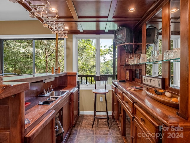 bar with beamed ceiling, sink, coffered ceiling, a notable chandelier, and wood counters