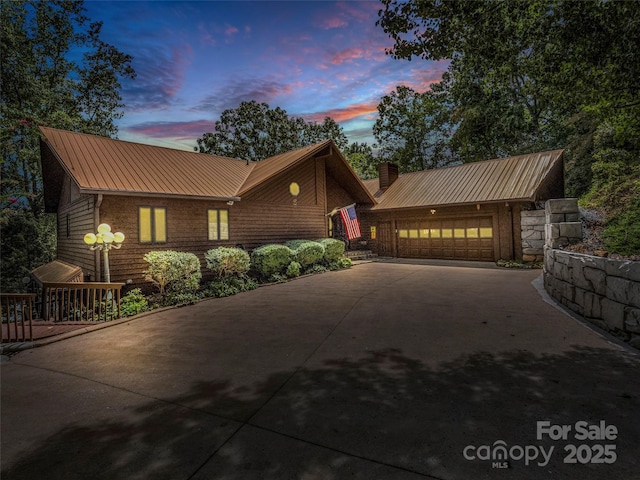 chalet / cabin featuring a chimney, concrete driveway, an attached garage, a standing seam roof, and metal roof