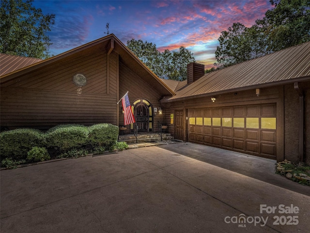 view of front of property featuring metal roof, concrete driveway, a chimney, and a garage